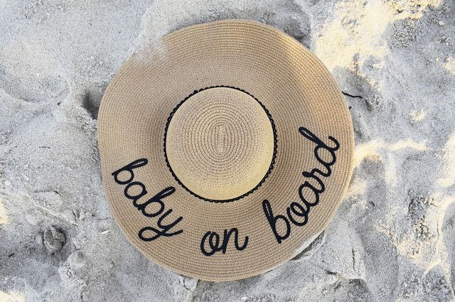 Best of Baby Travel Gear, a large sun hat sitting on sand with the boards baby on board written on the hat in black, cursive lettering.